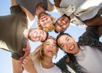 Cheerful friends huddling against blue sky on sunny day